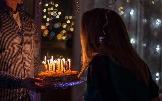 A birthday cake with lit candles carried in the dark